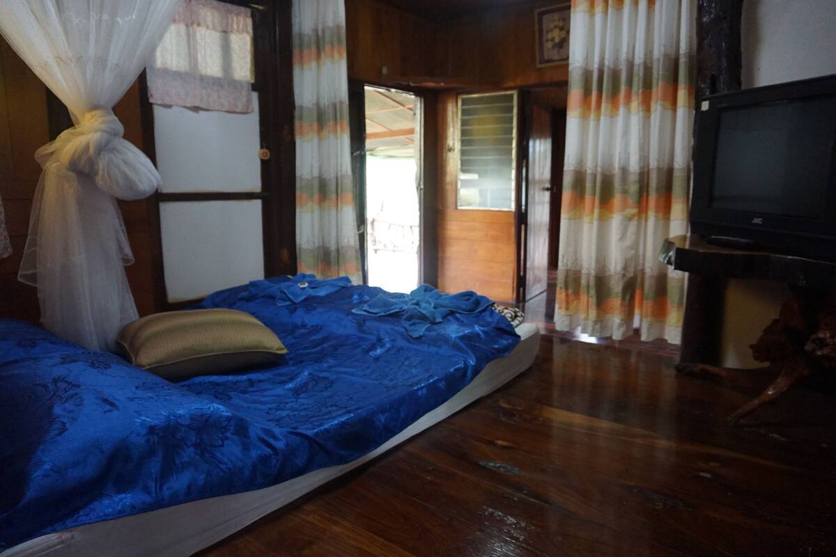 Ein Zimmer mit einem Bett, einem Fernseher und einer zur Außenwelt führenden Tür.