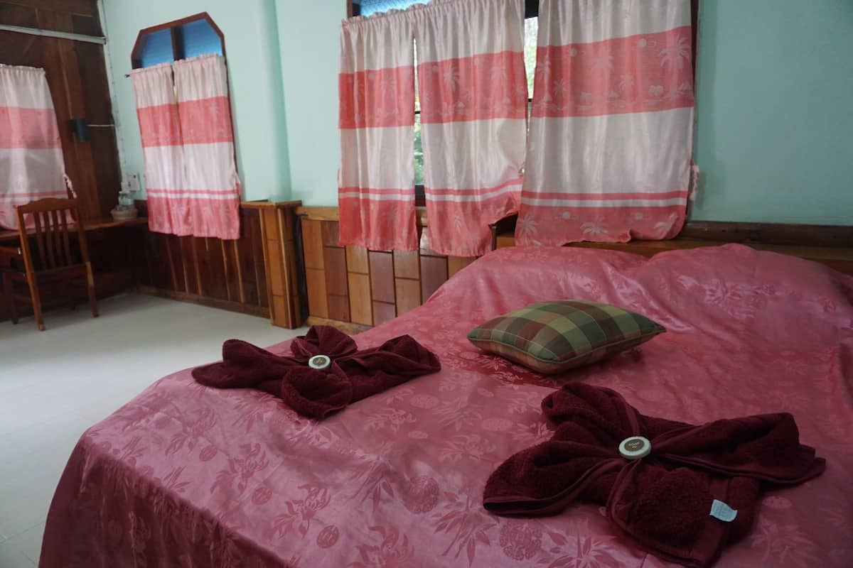 Ein Schlafzimmer mit einem Bett, zwei Handtüchern, einem Kopfkissen und Vorhängen.