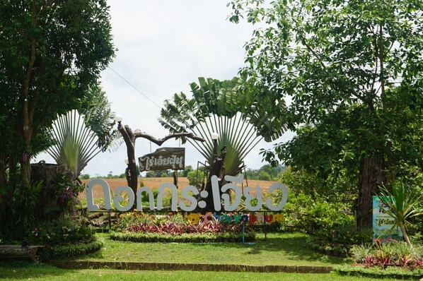A sign with Thai text in a garden setting.