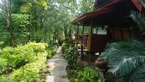 A wooden structure with a porch, surrounded by lush greenery and a concrete path. - Rai Aeifoon Resort (Thep Sathit)