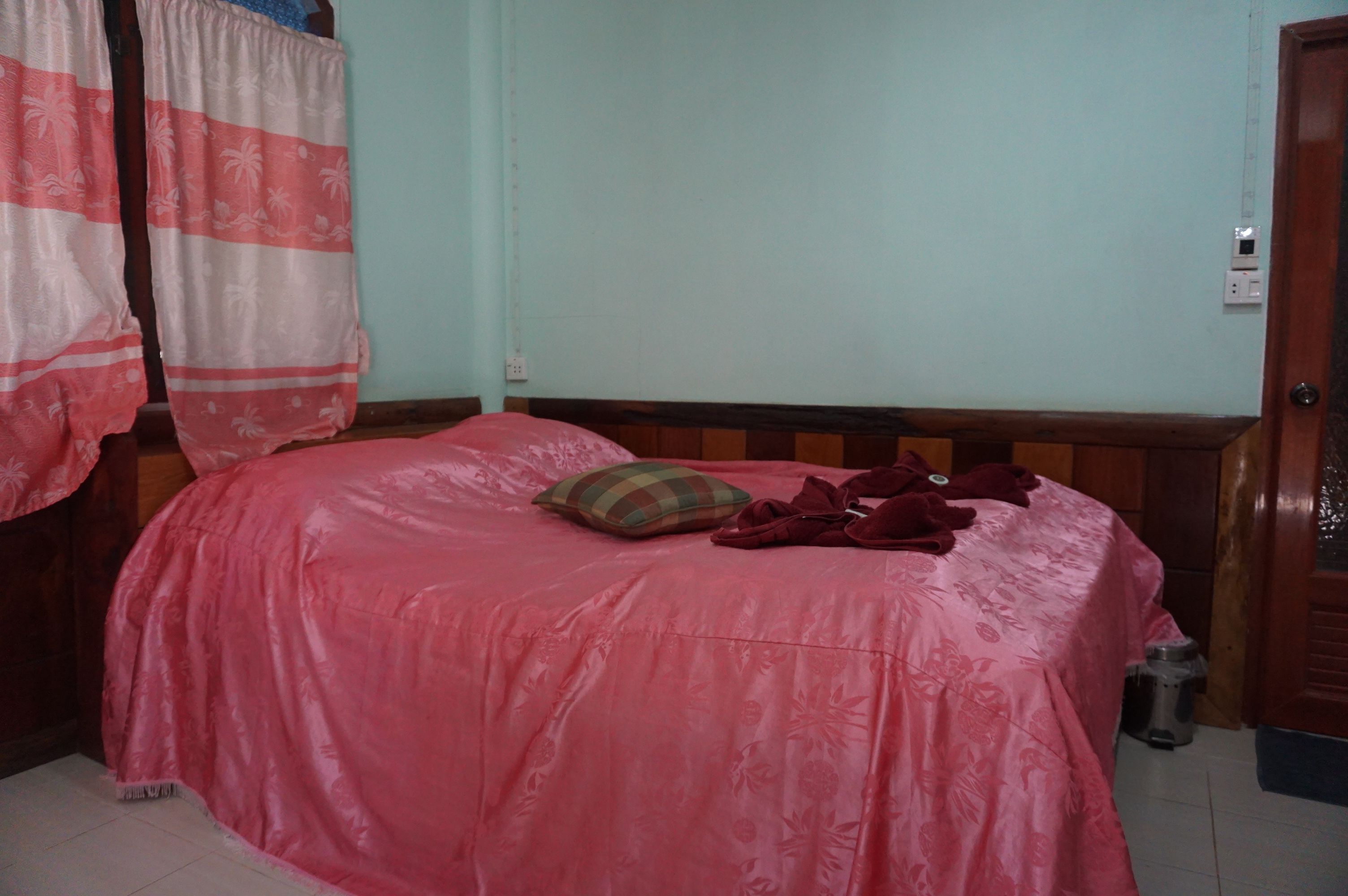 Una habitación con una cama cubierta por una colcha rosa, un cabecero de madera, un almohadón y una manta roja.