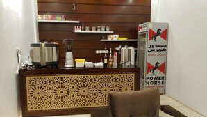 A reception area with a counter, a coffee machine, a blender, and a refrigerator. There are shelves with various items and a decorative panel.