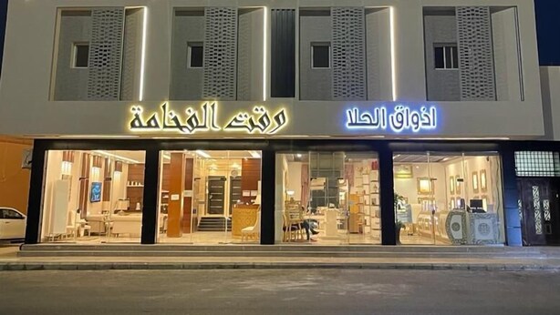 A modern building with illuminated signage in Arabic, featuring a clean, geometric facade and large windows.