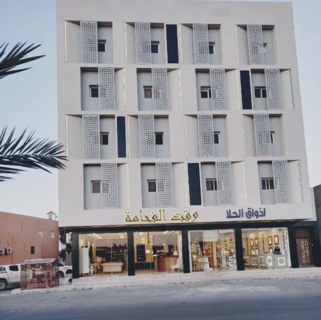 A multi-story building with a modern design, featuring a storefront with glass windows and a sign in Arabic.