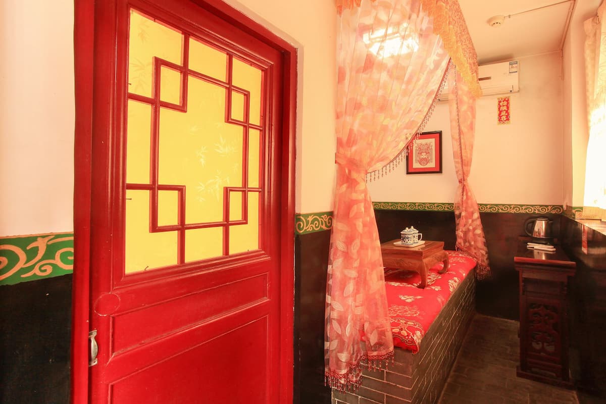 A traditional room with a red door, a bed with red bedding, a small table with a teapot, and a curtain.