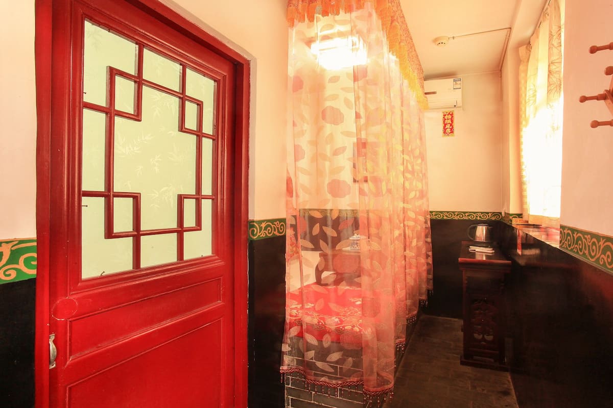 A narrow hallway with a red door featuring a traditional Chinese lattice design. A decorative curtain with leaf patterns hangs in the center.