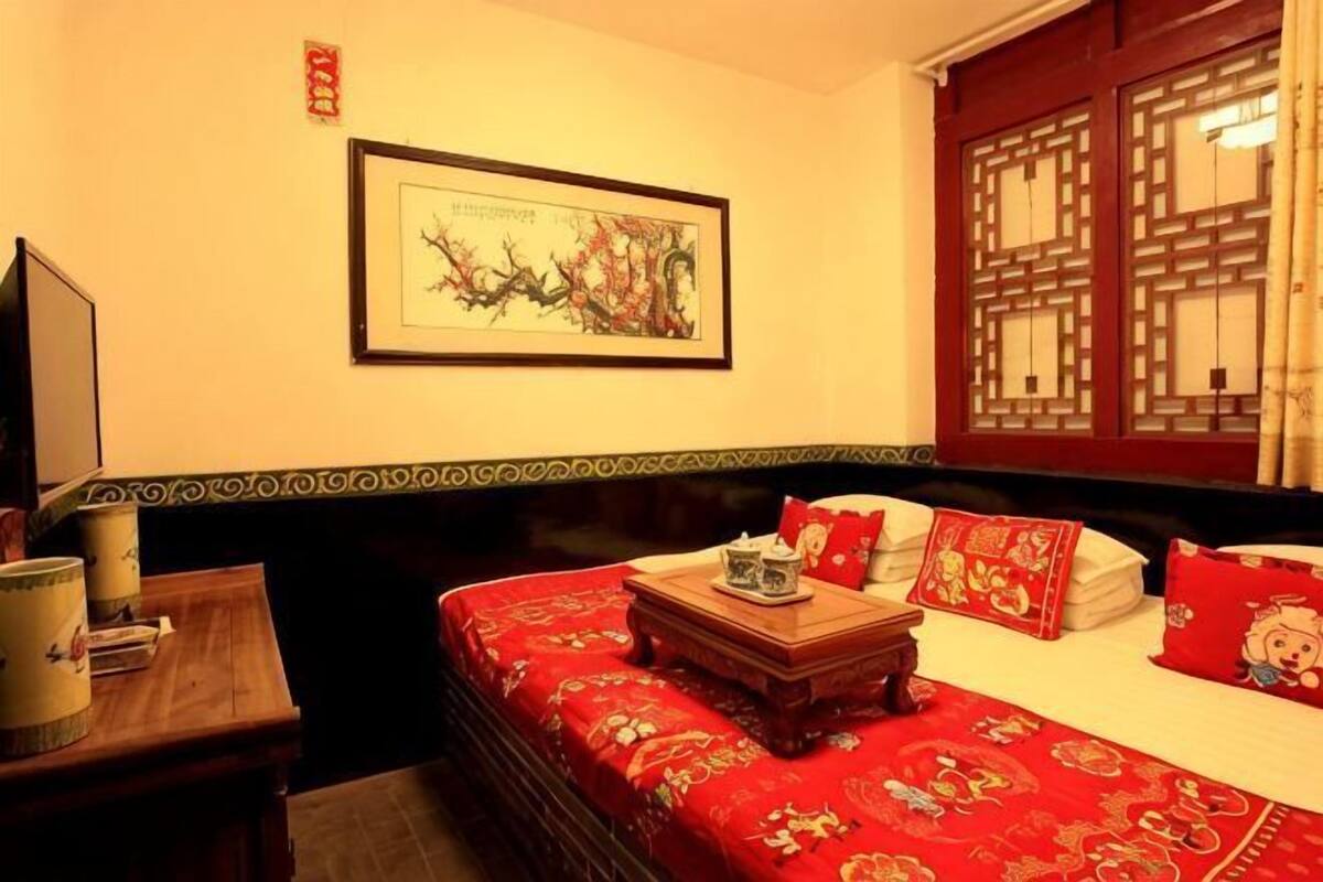 A hotel room with a bed, a television, a framed artwork, and a window with traditional Chinese lattice design.