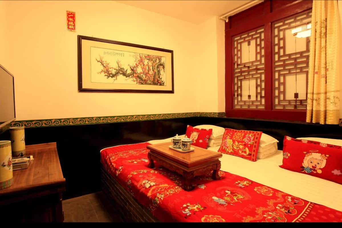 A traditional room with a bed, a wooden nightstand, a framed artwork, and a window with a lattice design.