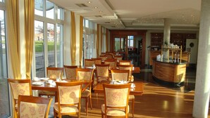 Un vaste espace dédié à la salle à manger, avec des tables et des chaises en bois, de grandes fenêtres et une vue sur l’extérieur.
