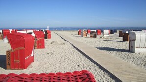 Une plage bordée de rangées de cabanes de plage rouges et blanches, le long d’un sentier sablonneux.