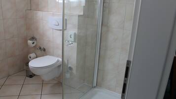 Ein Badezimmer mit Toilette, einer Duschkabine und Fliesenboden.