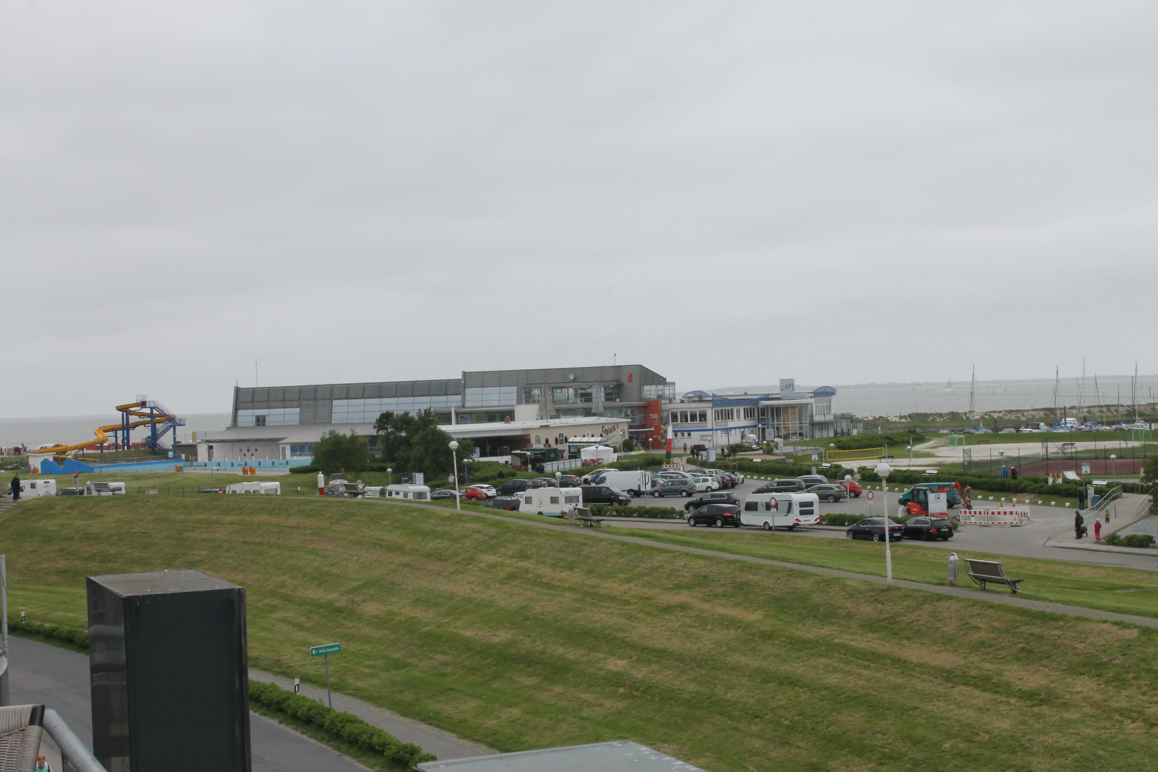 A parking lot with various vehicles, a grassy hill, and a building with multiple windows and a flat roof.