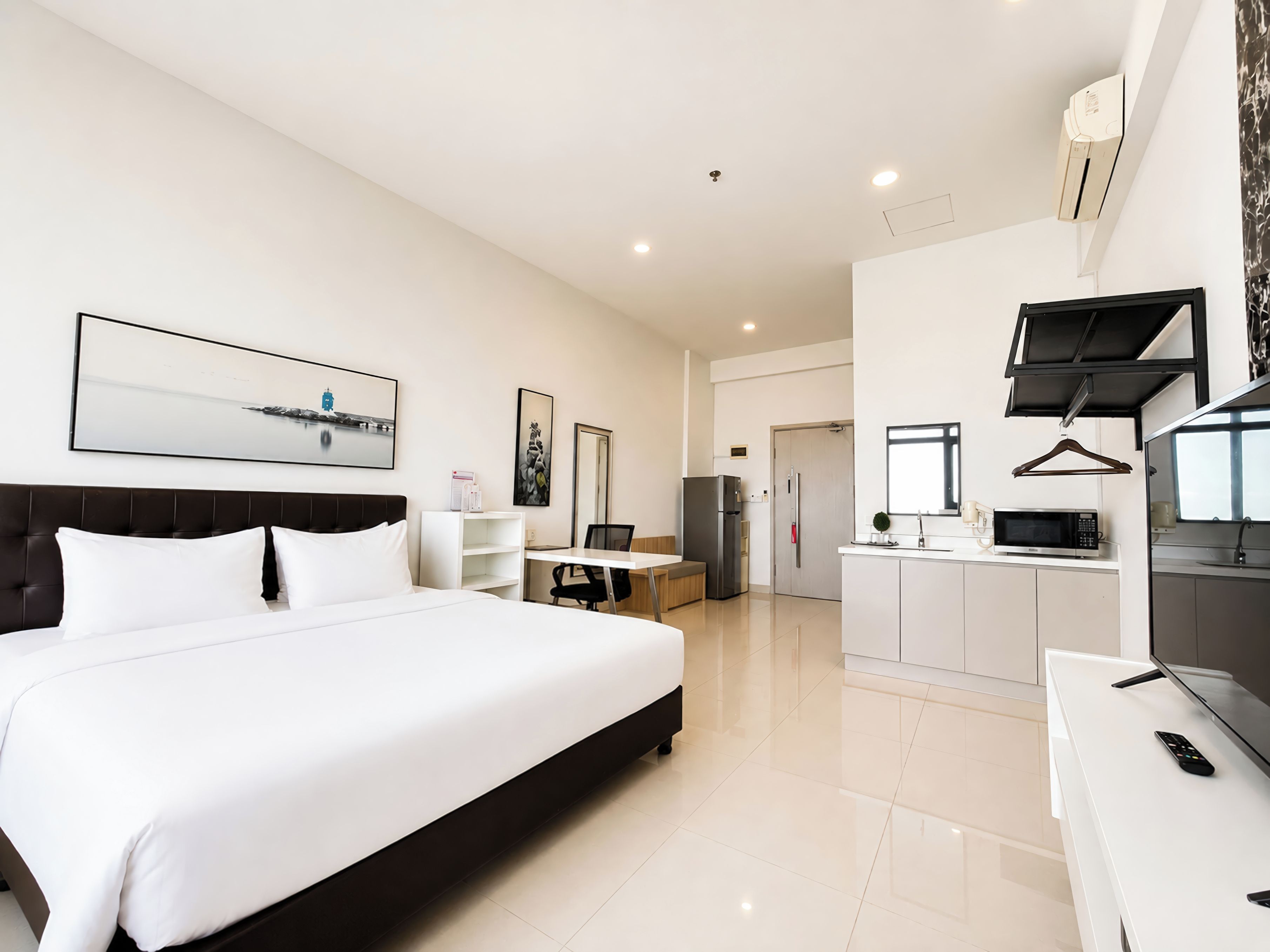 A modern hotel room with a large bed, a desk, a kitchenette, and a dining area.