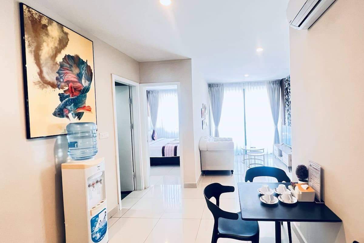A hotel room with a bed, a dining area with a table and chairs, a water dispenser, and a large painting on the wall.