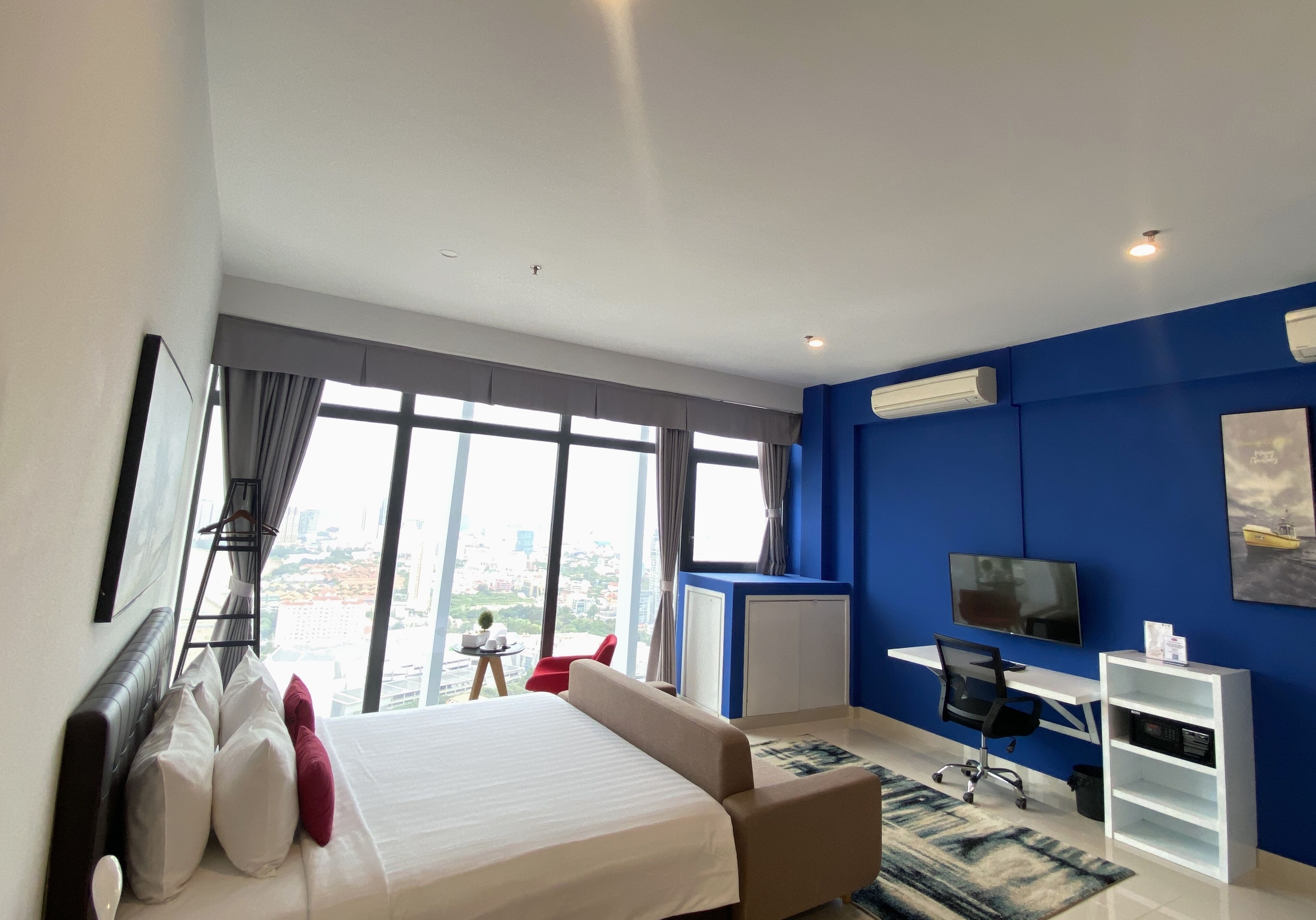 A modern hotel room with a large bed, a desk, a chair, a TV, and a view of the city.