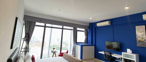 A modern hotel room with a large bed, a desk, a chair, a TV, and a view of the city.