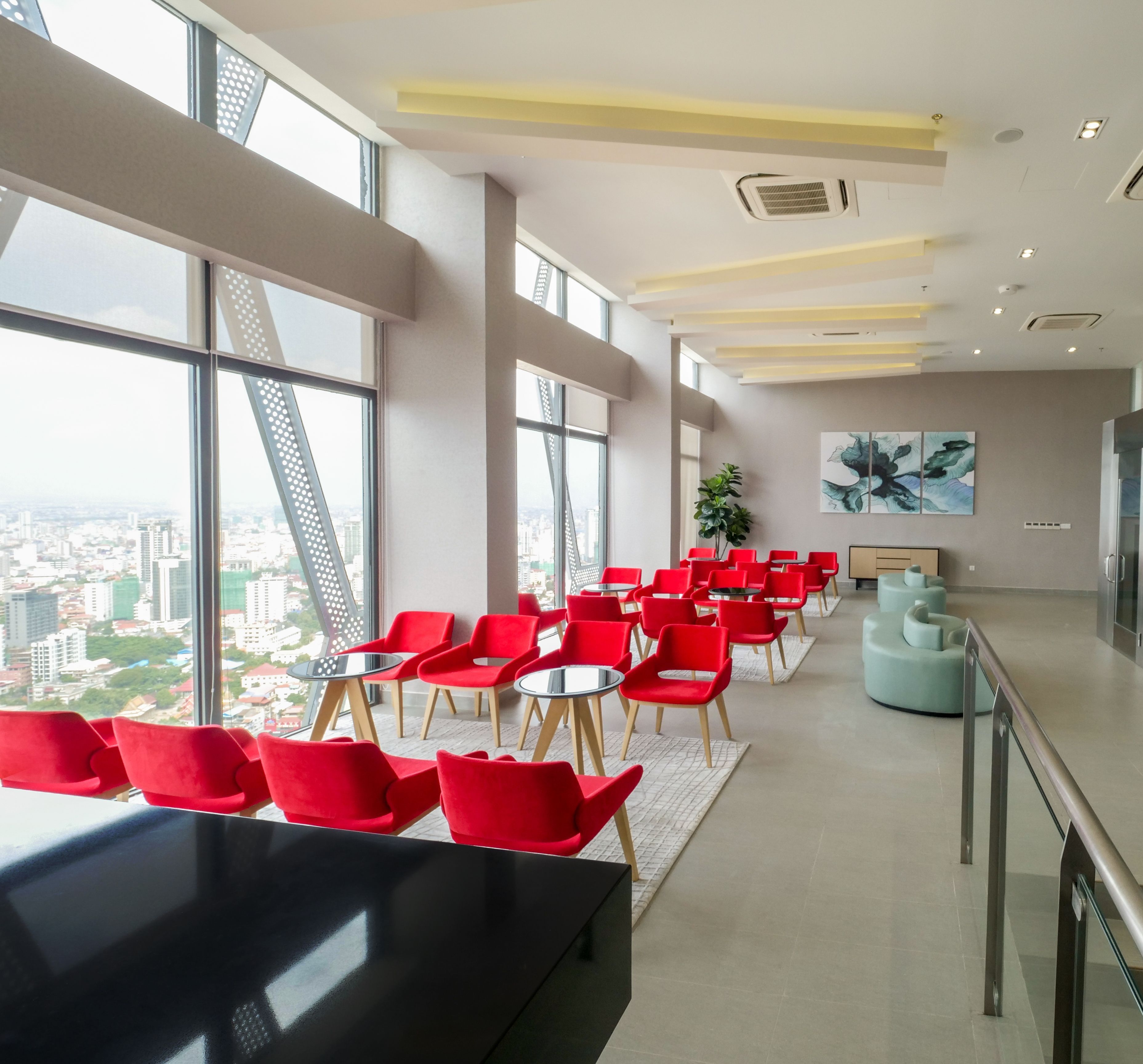 A modern conference room with red chairs and a black table, large windows with a city view, and a ceiling with recessed lighting.