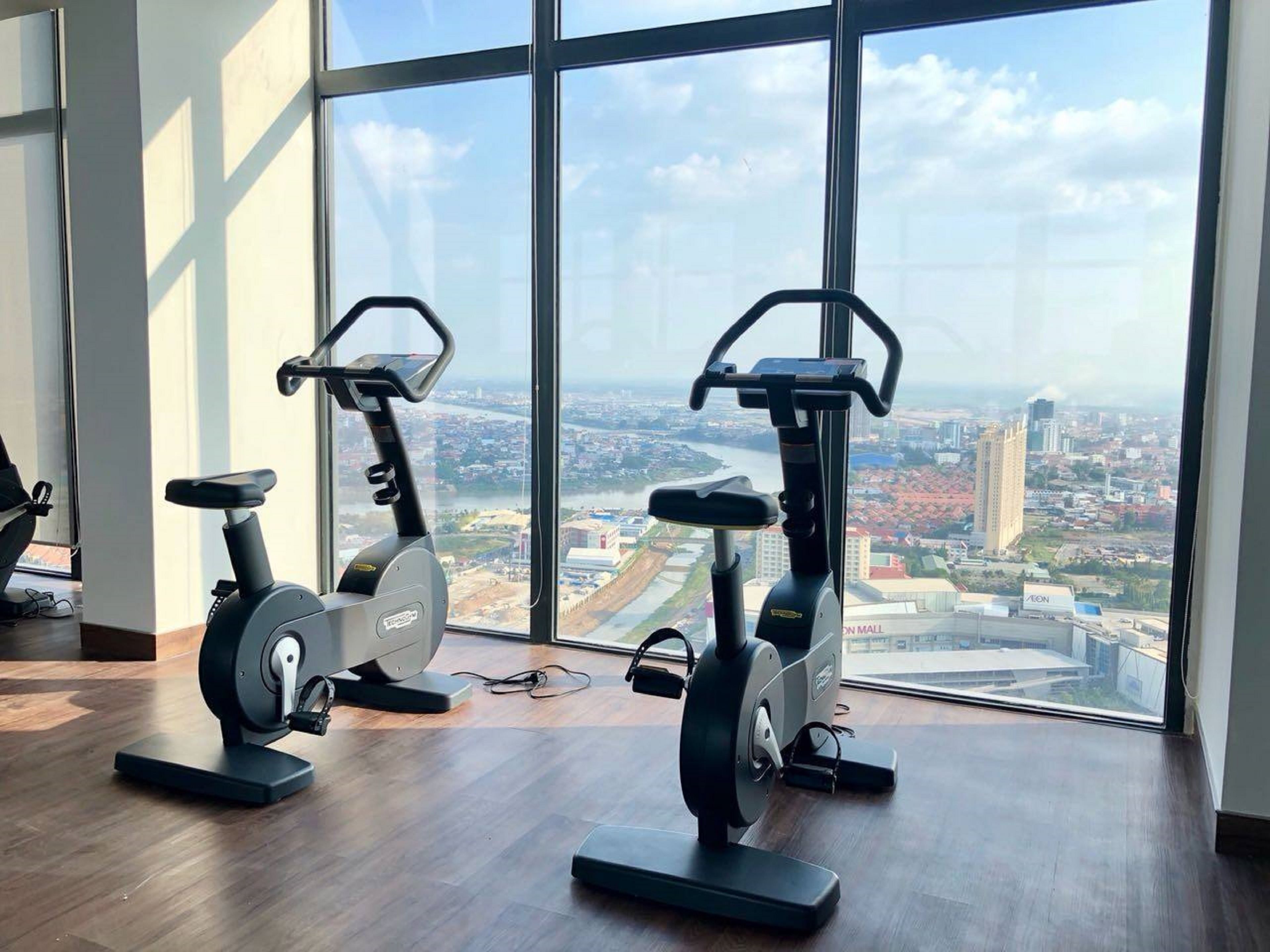 Deux vélos d’appartement sont placés dans une pièce dotée de grandes fenêtres donnant sur un paysage urbain.