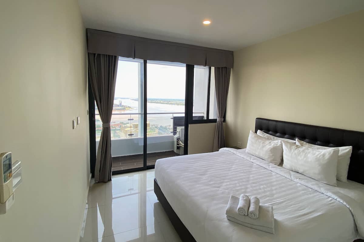 A hotel room with a large bed, a view of the city, and a balcony with curtains.