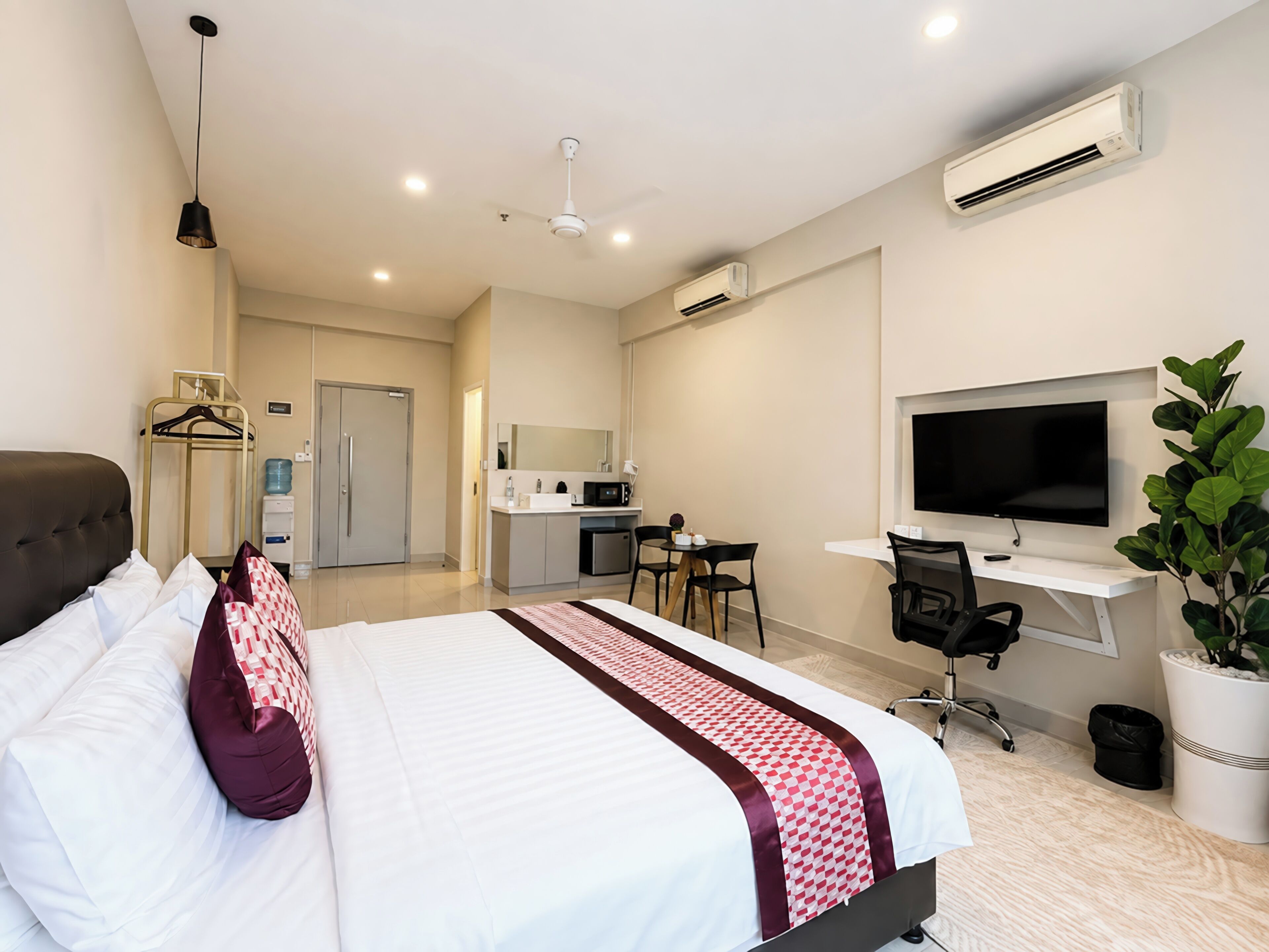 A hotel room with a bed, desk, TV, and a kitchenette.