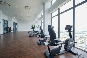 A gym with cardio machines, large windows, and a wooden floor.