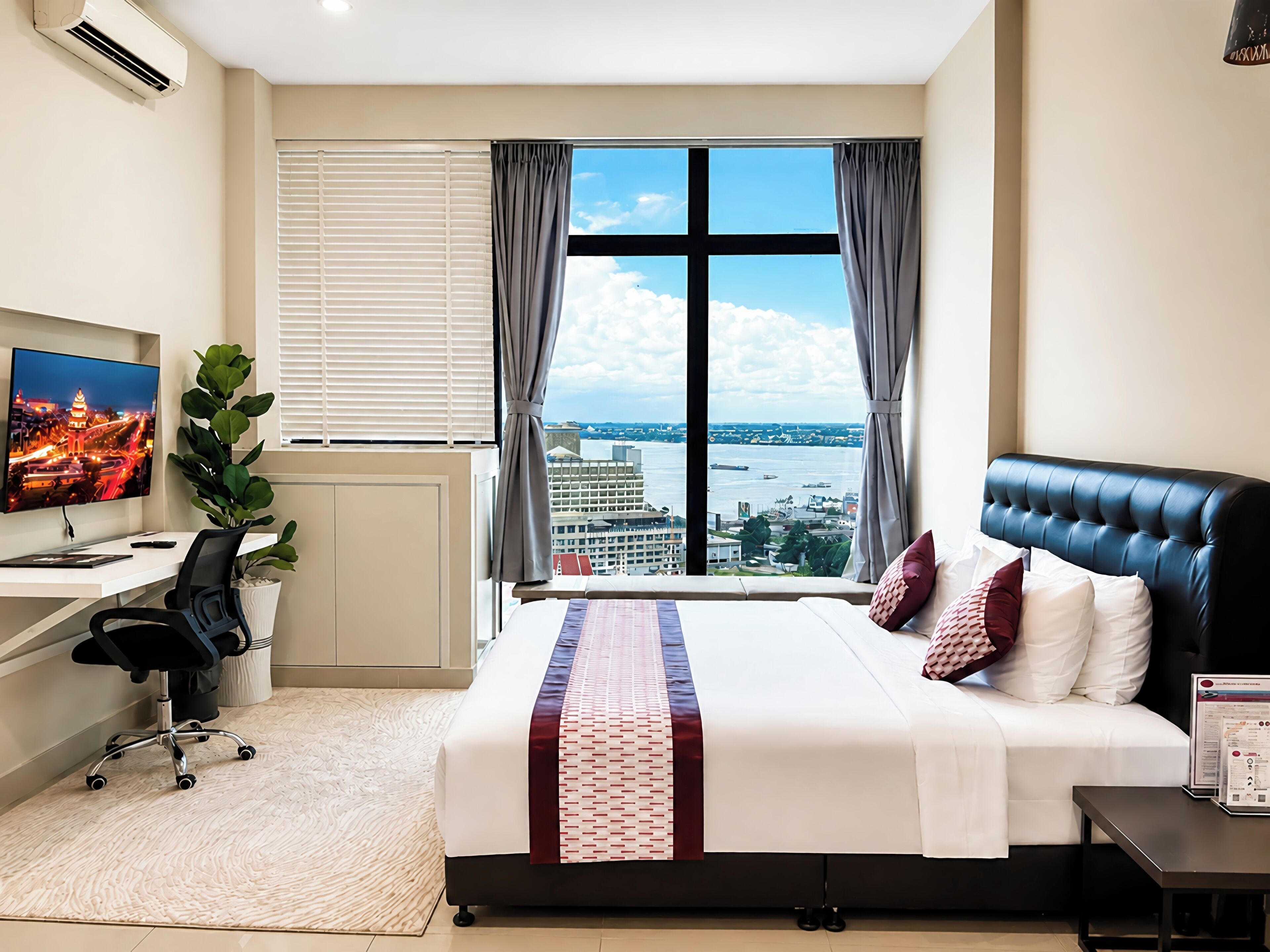 Ein Hotelzimmer mit einem großen Bett, einem Schreibtisch mit Computer, einem Fernseher und Blick auf die Stadt.