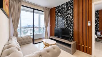Un salón moderno con un televisor de pantalla plana grande, un sofá cómodo, una mesa redonda pequeña y vistas de la ciudad a través de ventanales de techo a suelo.