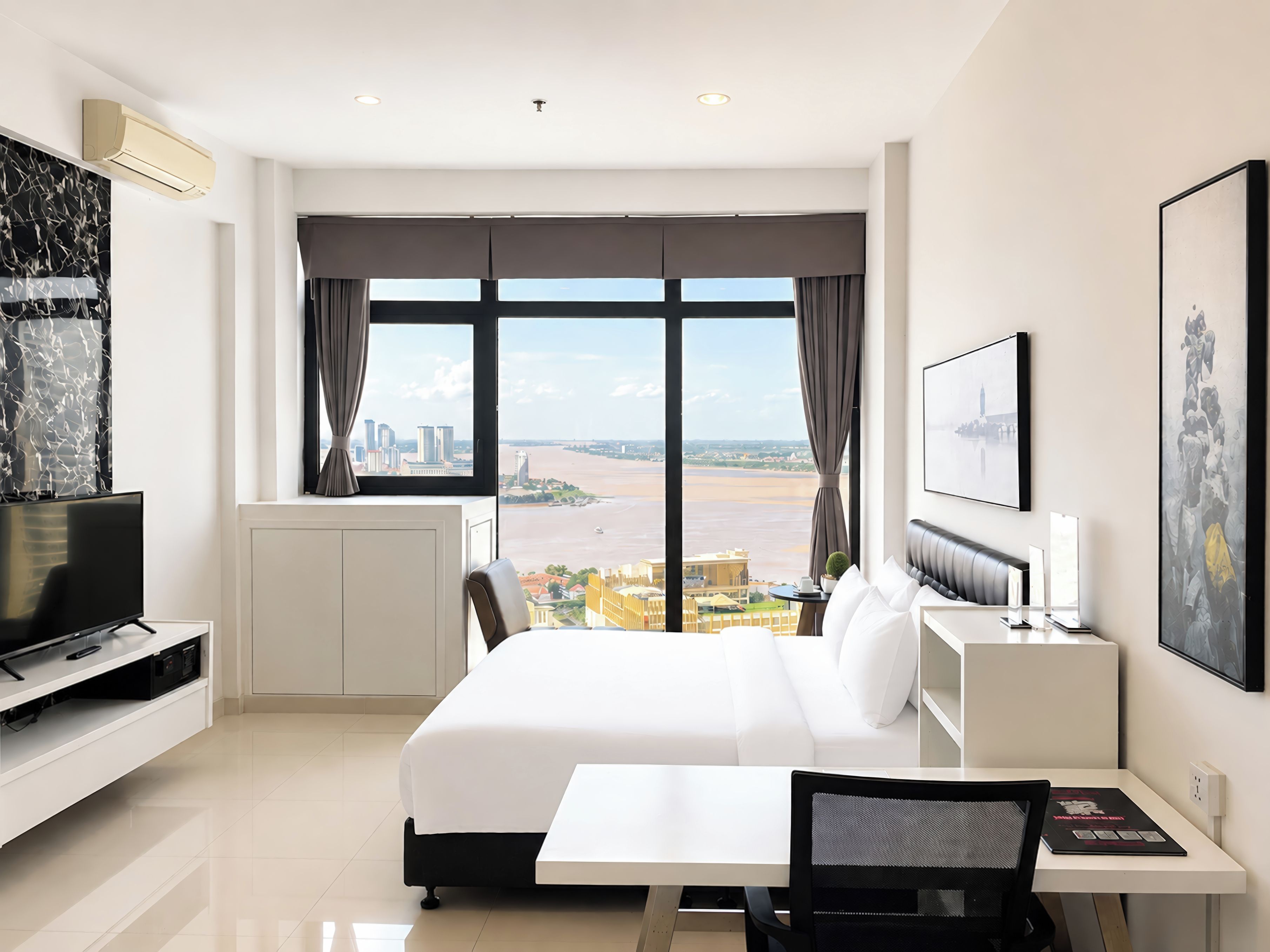 Habitación de hotel con cama, escritorio, televisor y ventana grande con vista a la ciudad.
