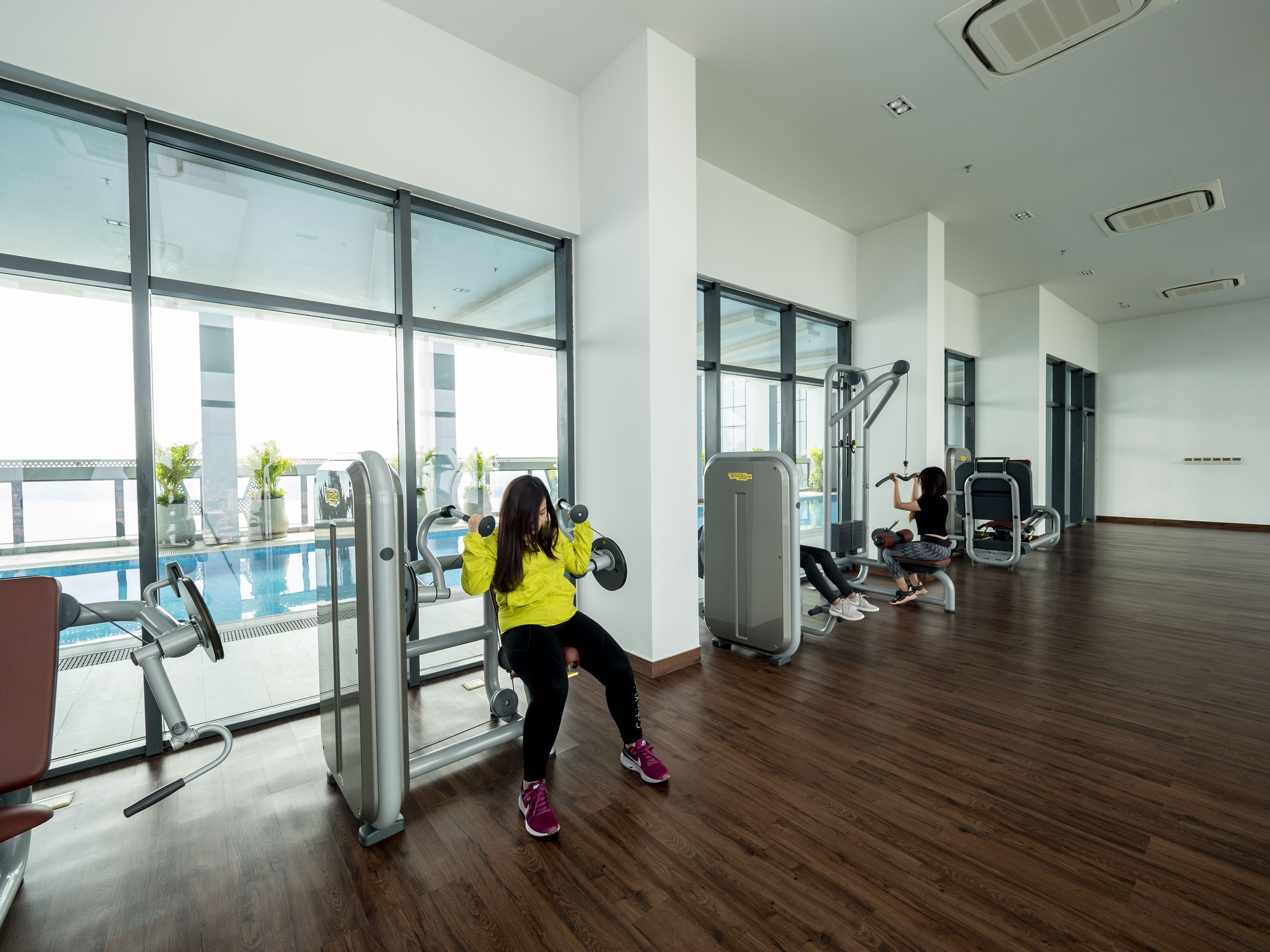Un gimnasio con equipo de ejercicio, ventanas amplias y vistas a la piscina.