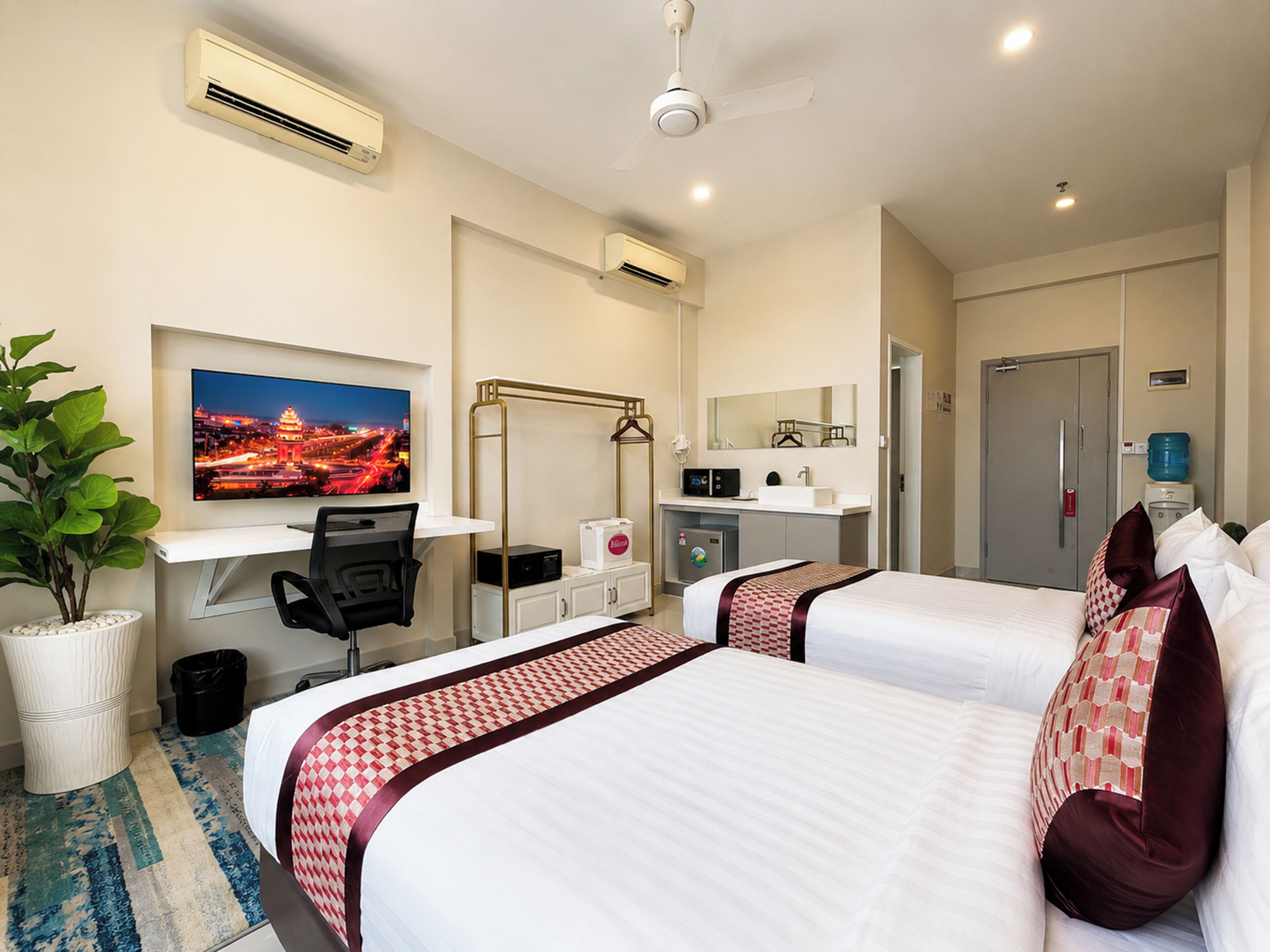 Ein Hotelzimmer mit zwei Betten, einem Schreibtisch, einem Fernseher, einer Minibar und einem Badezimmer.