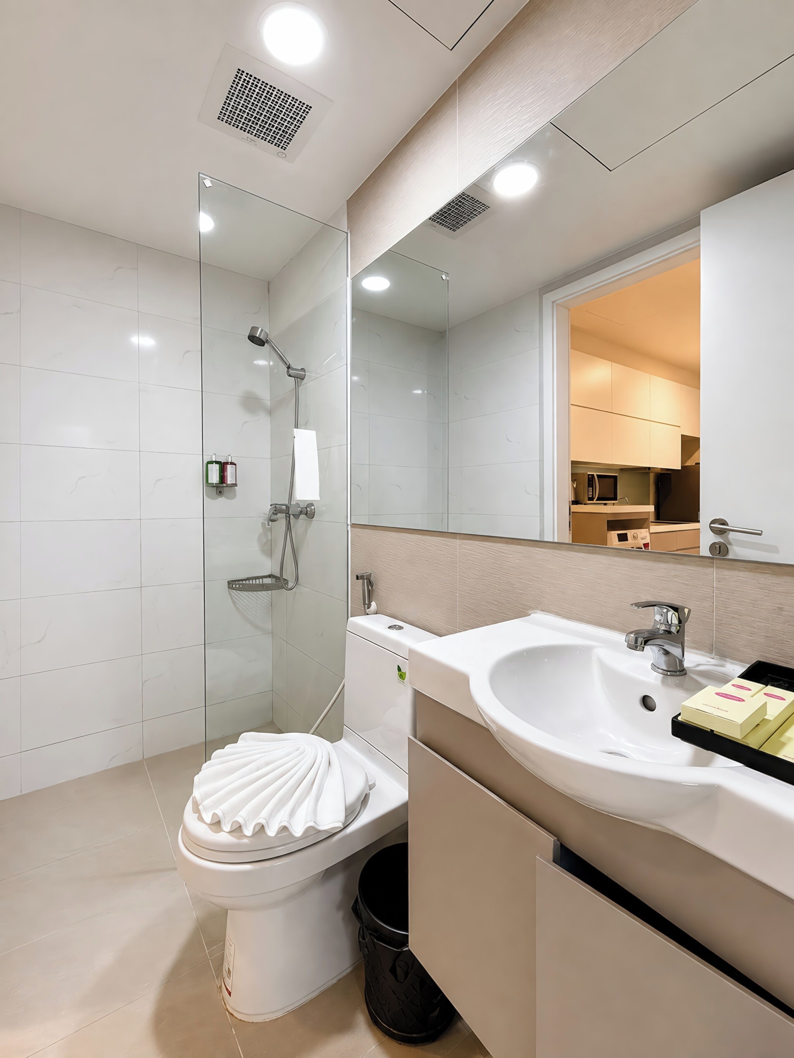 Un baño moderno con ducha de vidrio, inodoro blanco y lavabo con espejo superior.