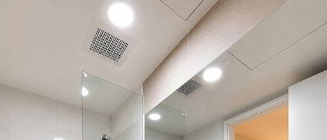 A modern bathroom with a glass-enclosed shower, a white toilet, and a sink with a mirror above.