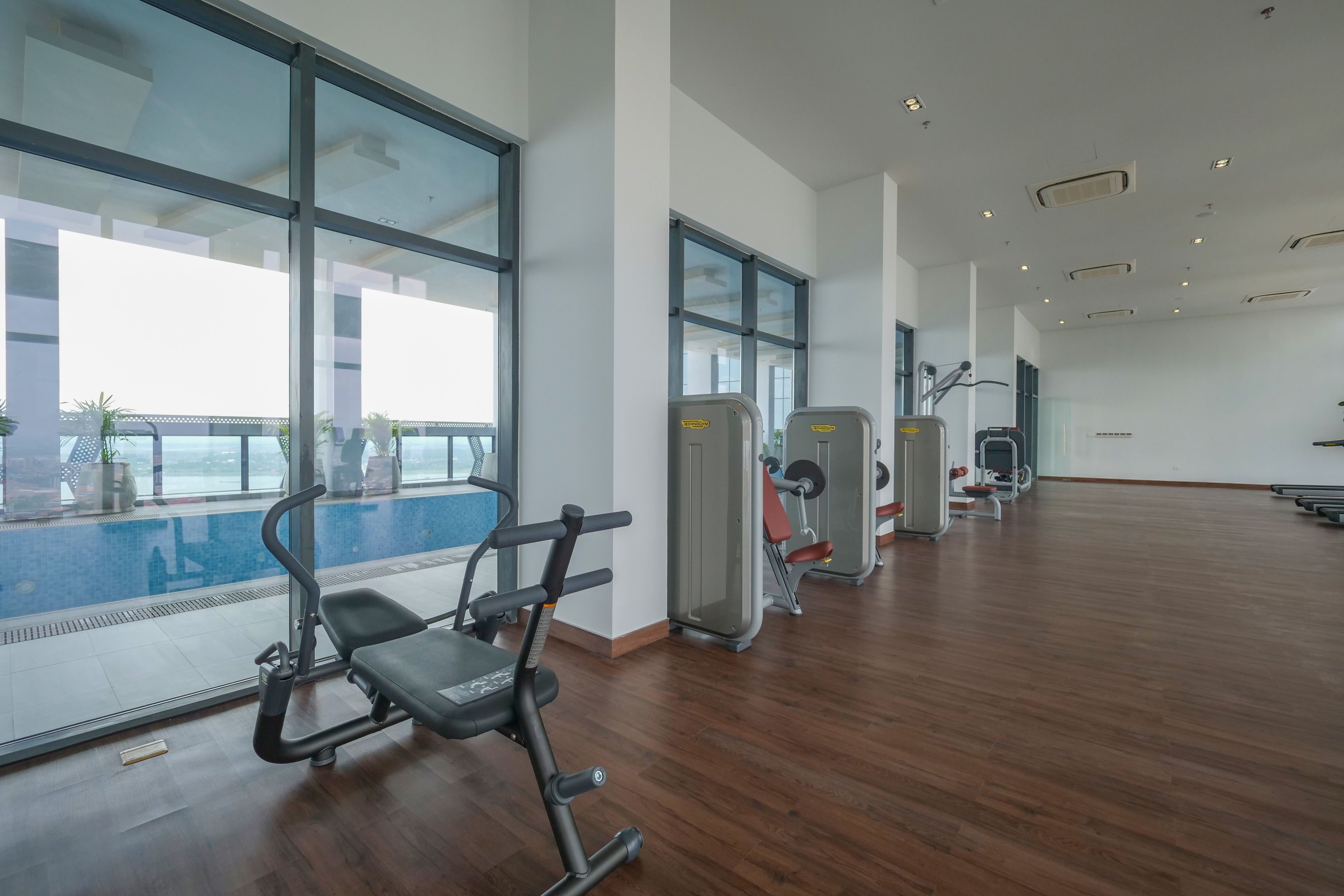 Ein geräumiger Fitnessraum mit großen Fenstern, Holzböden und verschiedenen Trainingsgeräten.
