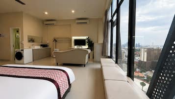 Habitación de hotel con cama, sofá, televisor, lavadora y vista a la ciudad.