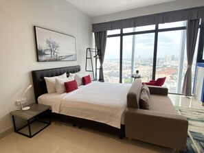 A modern hotel room with a large bed, a sofa, a desk with a lamp, a view of the city through large windows, and a painting on the wall. - The Bridge Club (Phnom Penh)