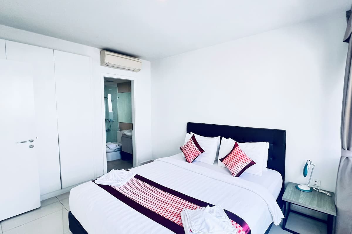 A hotel room with a bed, a nightstand, a window with curtains, a wardrobe, and a bathroom visible through an open door.