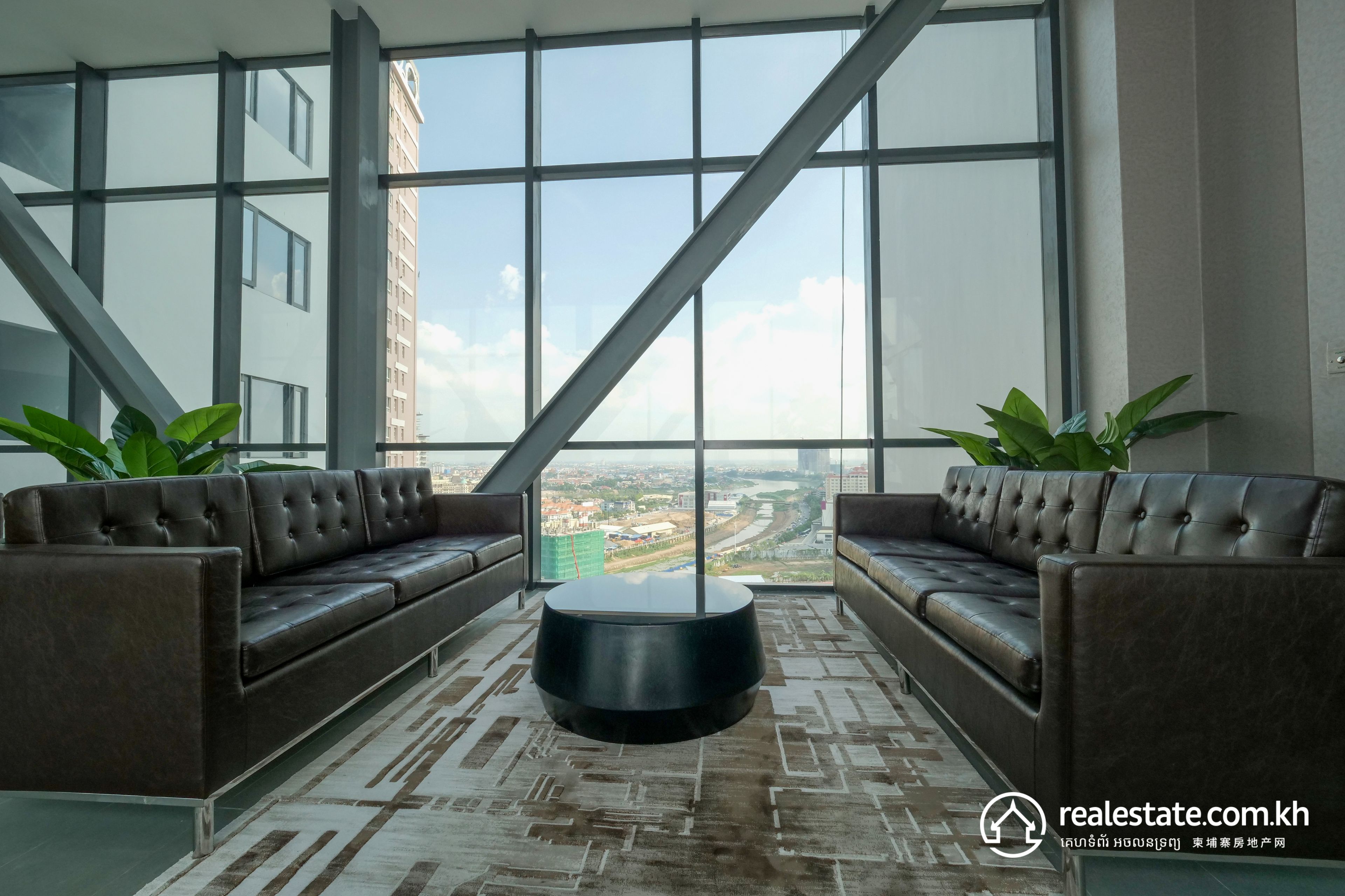 A modern interior with two leather sofas facing a large window, a central round table, and a patterned floor.