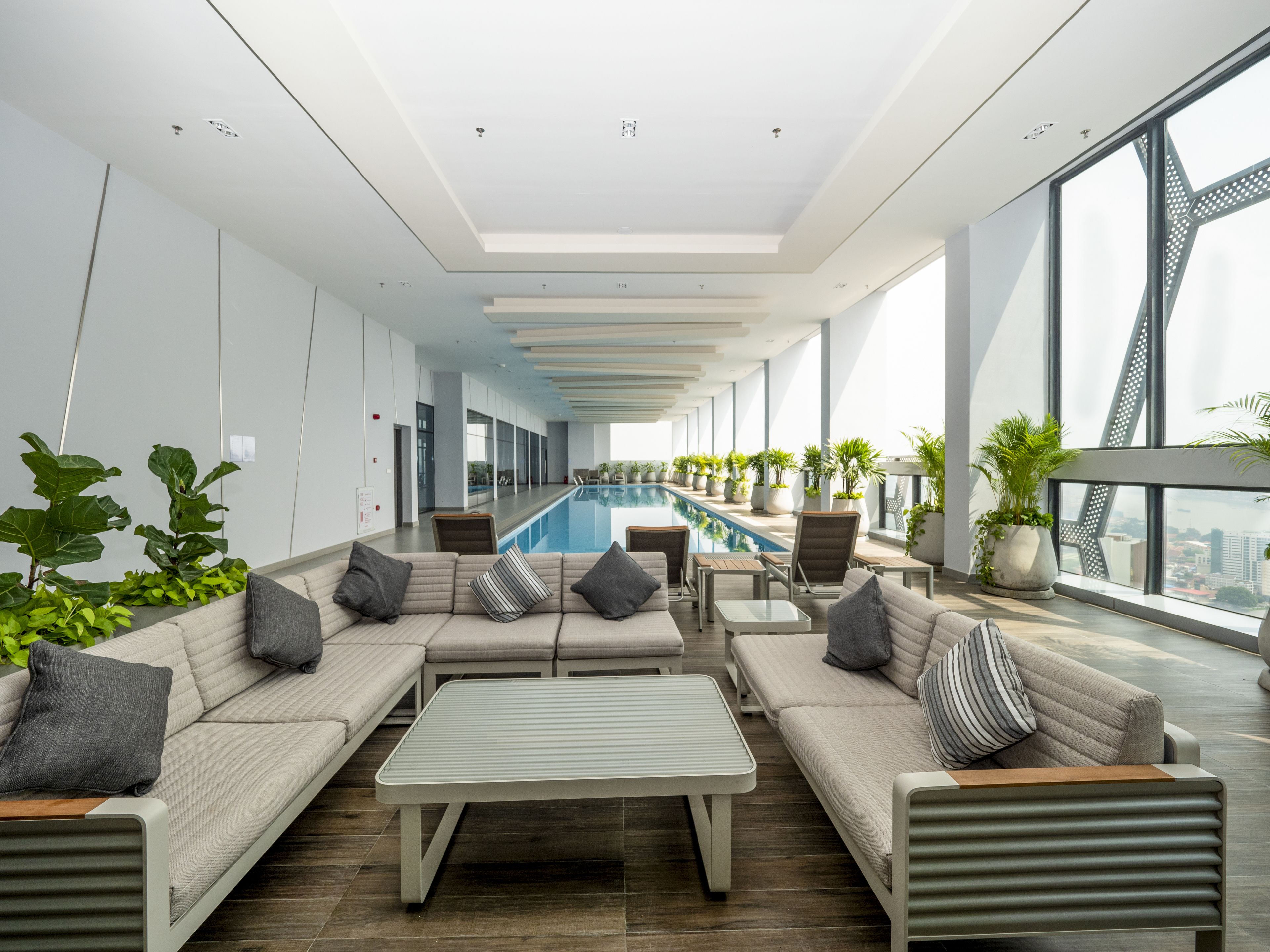 A modern indoor pool area with seating and potted plants.