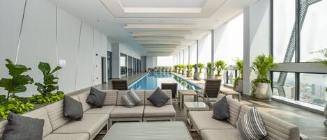 A modern indoor pool area with seating and potted plants.