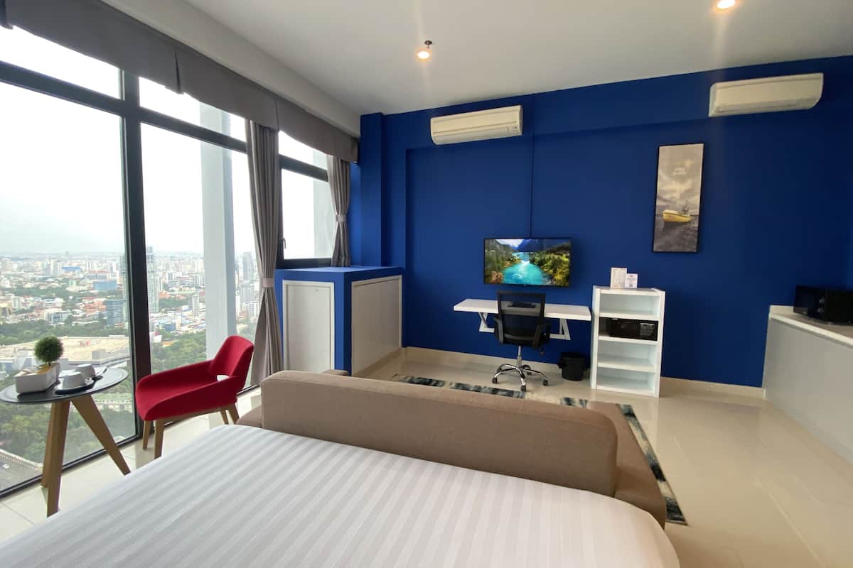 A modern hotel room with a large bed, a desk with a chair, a TV, and a view of the city.