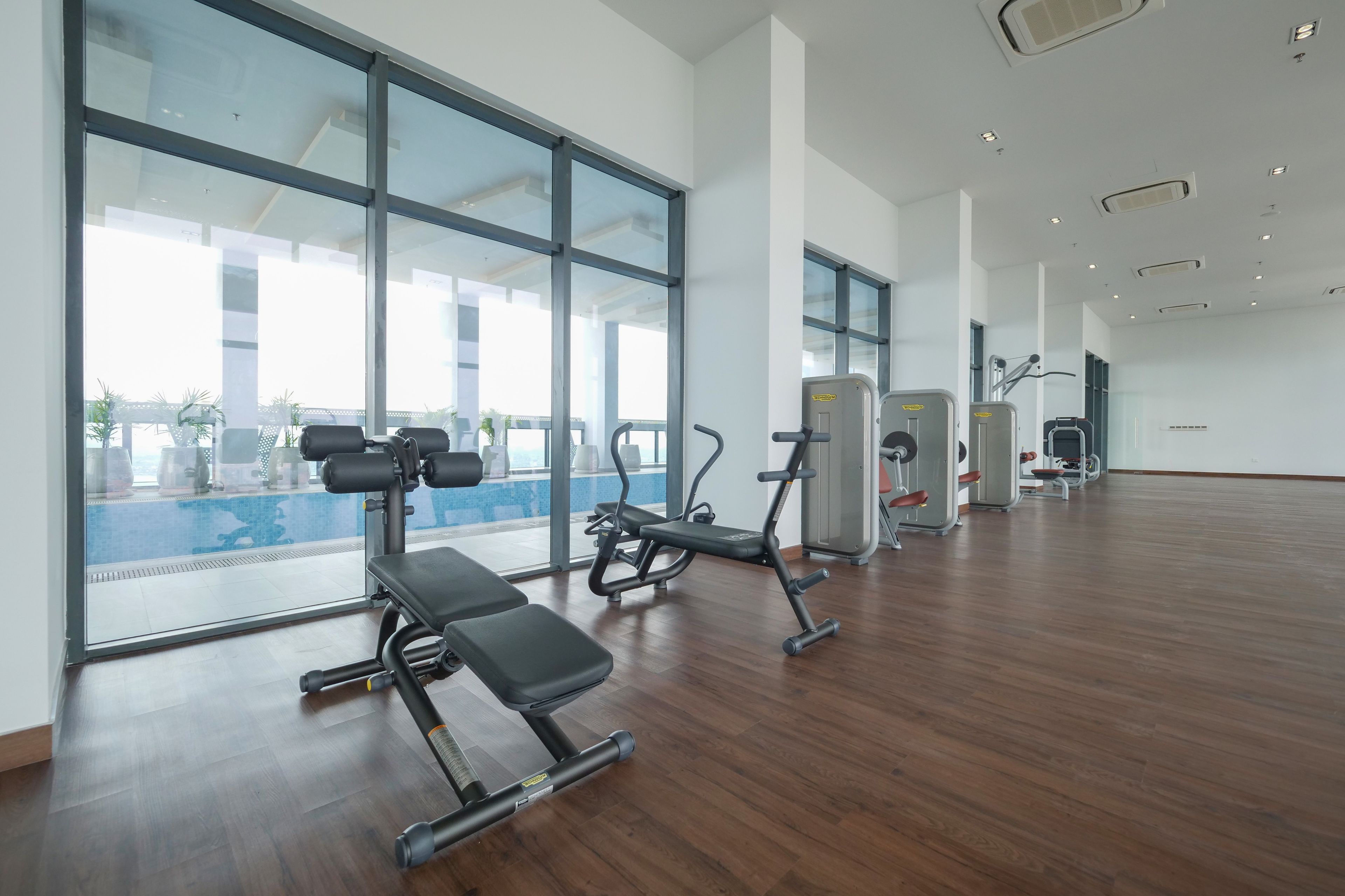 A spacious gym with large windows, wooden flooring, and various exercise equipment.