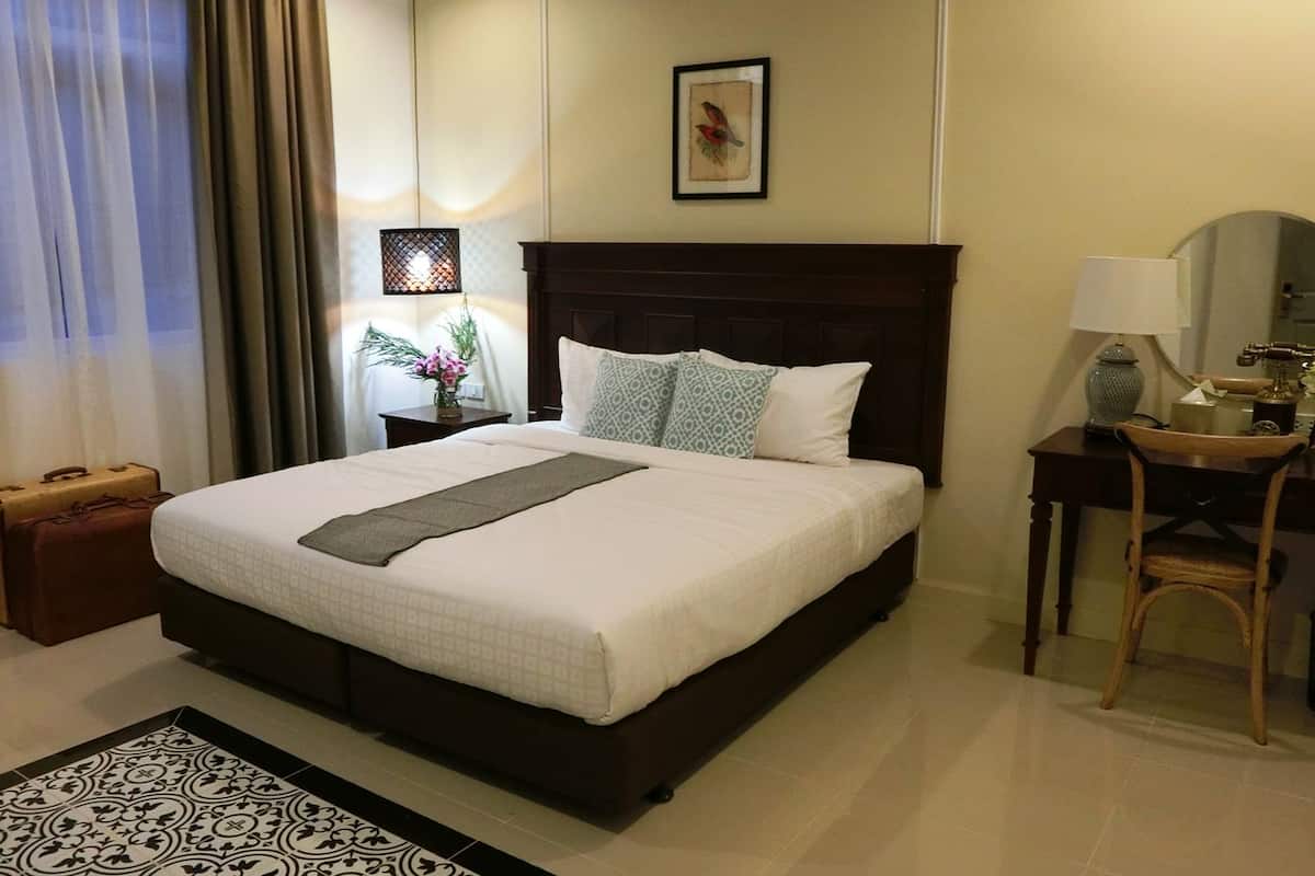 A neatly made bed with a patterned bedspread and pillows, a bedside table with a lamp, a small vase with flowers, and a framed picture on the wall.
