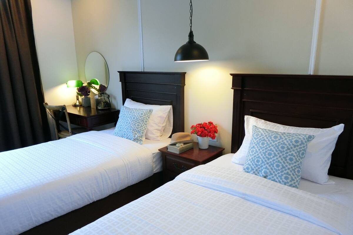 A hotel room with two beds, a nightstand, a lamp, and a mirror.