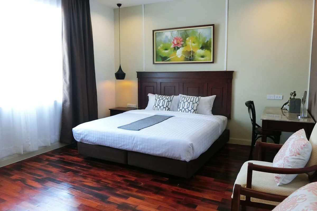 A hotel room with a large bed, a nightstand, a desk with a chair, and a painting on the wall.