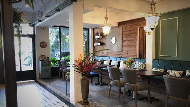 A modern interior with a dining area, a wooden accent wall, and a view of the outdoors. - Bloom Boutique Hotel and Cafe (Vientiane)