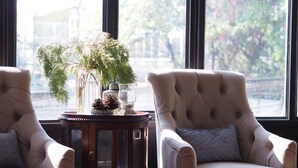 Two armchairs with a round wooden table between them, featuring decorative items and a view of the outdoors through large windows. - Bloom Boutique Hotel and Cafe (Vientiane)