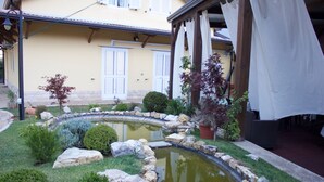 A courtyard with a small pond, potted plants, and a building with white shutters. - Ostello Villafranca (Pignola)