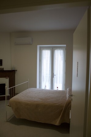 A bedroom with a bed, a fireplace, and a window with curtains. - Ostello Villafranca (Pignola)