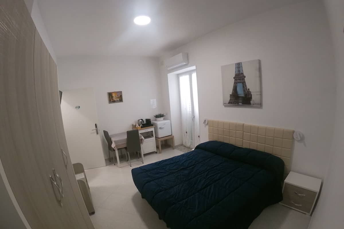 A bedroom with a bed, a desk, a chair, and a small cabinet.