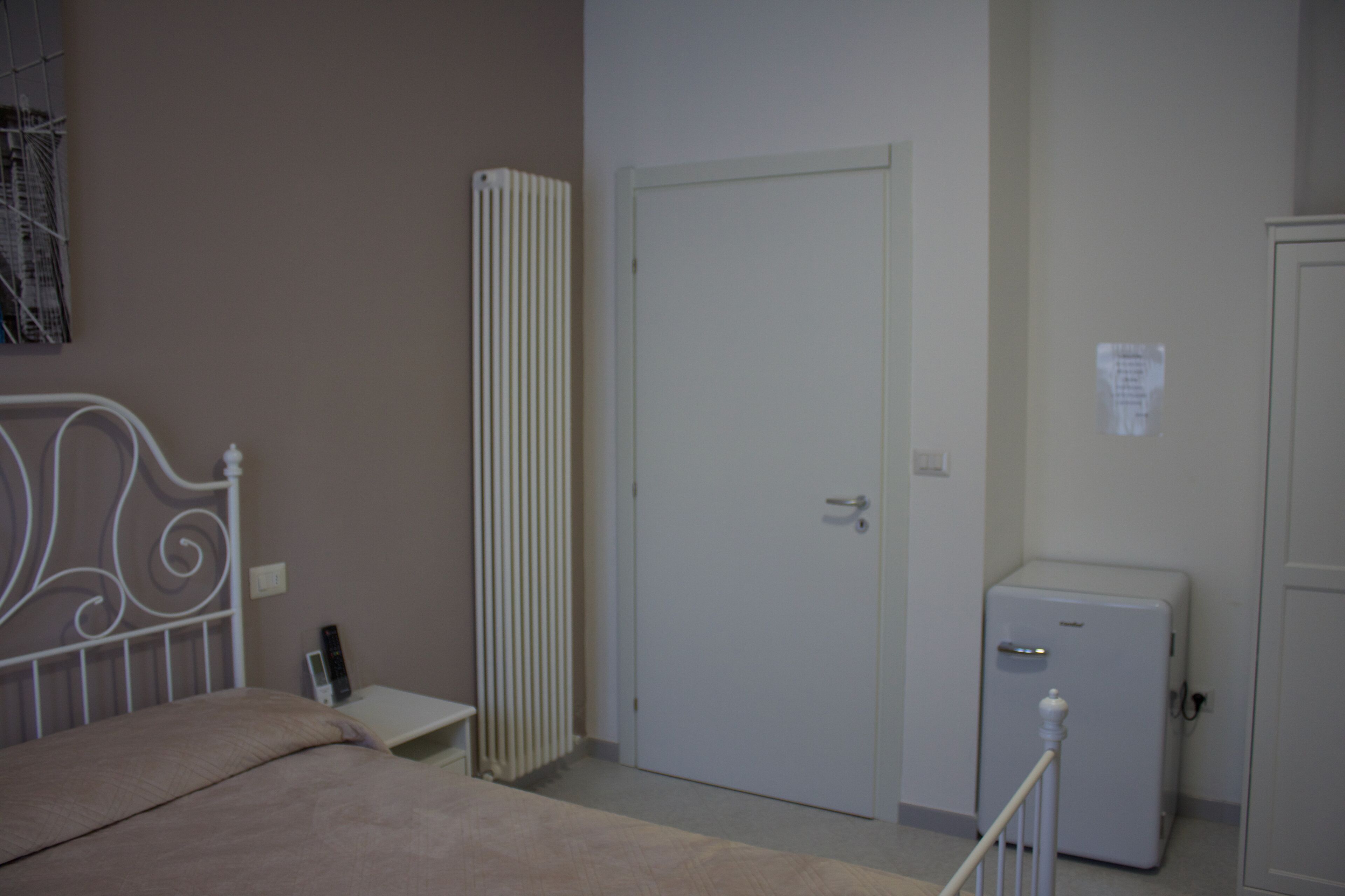 Une chambre avec un lit, un radiateur, une porte et un petit réfrigérateur.